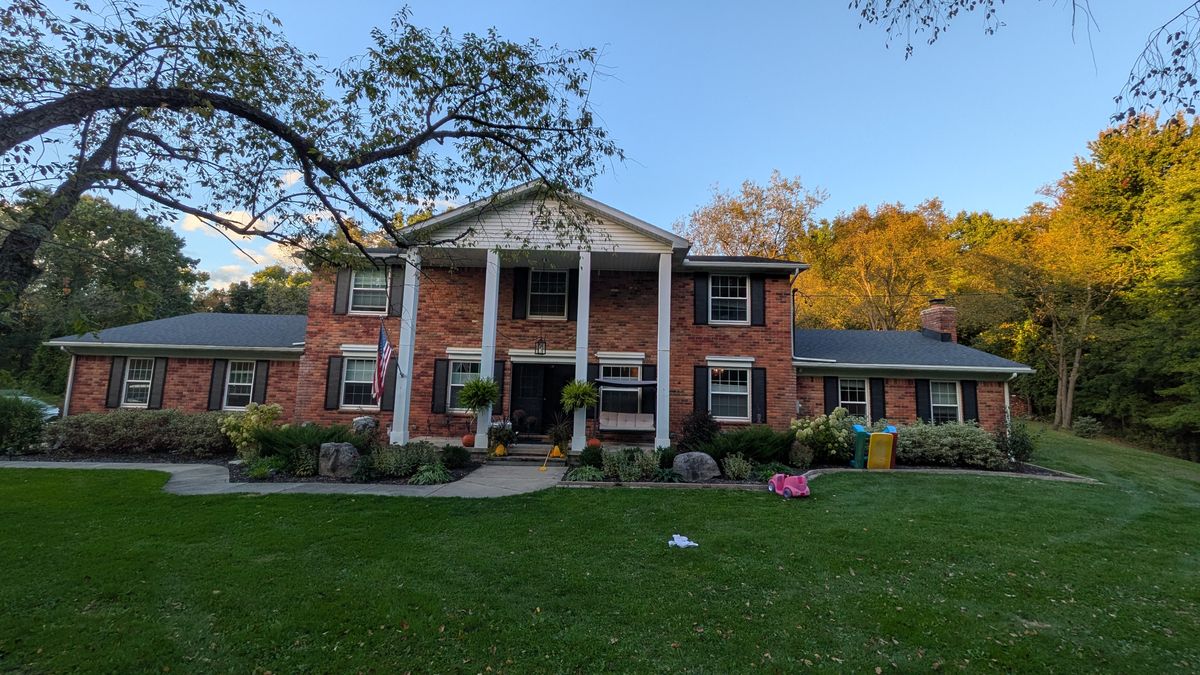 Front of the house: red brick, black shutters, a two-story portico with four white columns, and a lower wing on each side