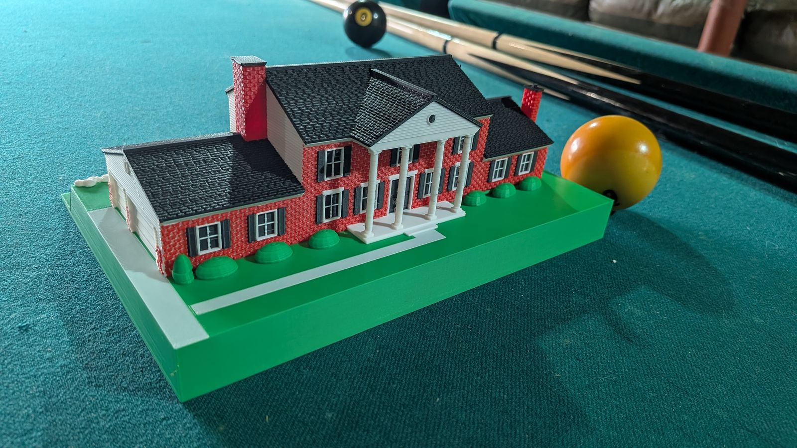 The finished HouseMini from the front corner: red brick, black shutters, a white-columned portico, black shingled roofs, and a green lawn base