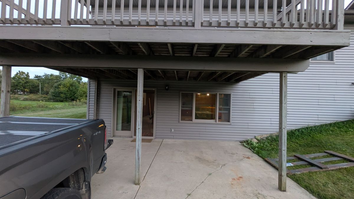 Under the deck at dusk: the posts, the patio, and the walkout door